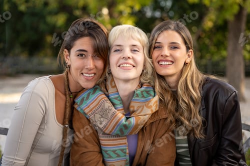 Preview: Portrait of three happy diverse young women, best friends smiling together outdoors in a park.