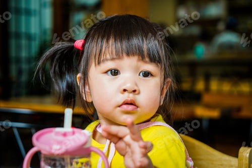 Preview: Little Caucasian girl sit at table at restaurant and look away with glass for children on the table.