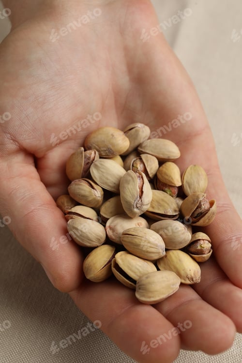 Preview: Woman holding tasty roasted pistachio nuts at table, closeup