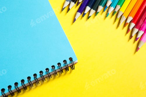 Preview: Rainbow palette of colored pencils with a spiral notebook on a yellow background