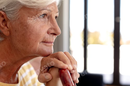 Preview: Caucasian senior woman holding a walking stick smiling sitting on the couch at home