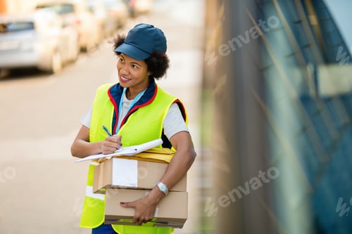 Preview: Smiling black delivery woman with packages filling paperwork on the street.