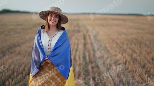 Preview: Smiling ukrainian woman with national flag in wheat field after harvesting. Charming rural lady
