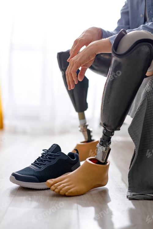 Preview: cropped man leg amputee wearing or changing prostheses at home sitting on bed