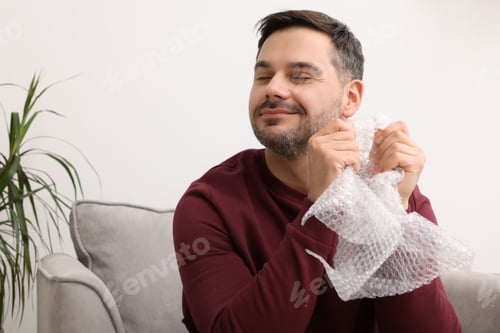 Preview: Happy man with bubble wrap indoors. Space for text