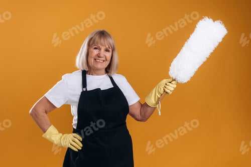 Preview: Ready to clean the house. Senior housewife is standing against background