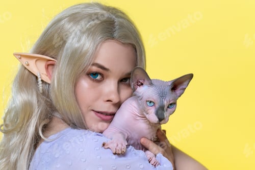 Preview: Portrait of cosplay elf young woman in summer blue dress holding Sphinx cat near cheek