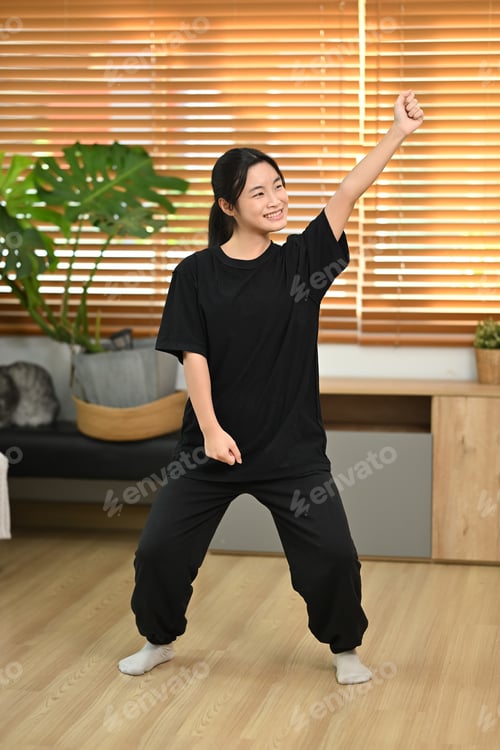 Preview: Cheerful young asian woman having fun, practicing a dance move in a living room