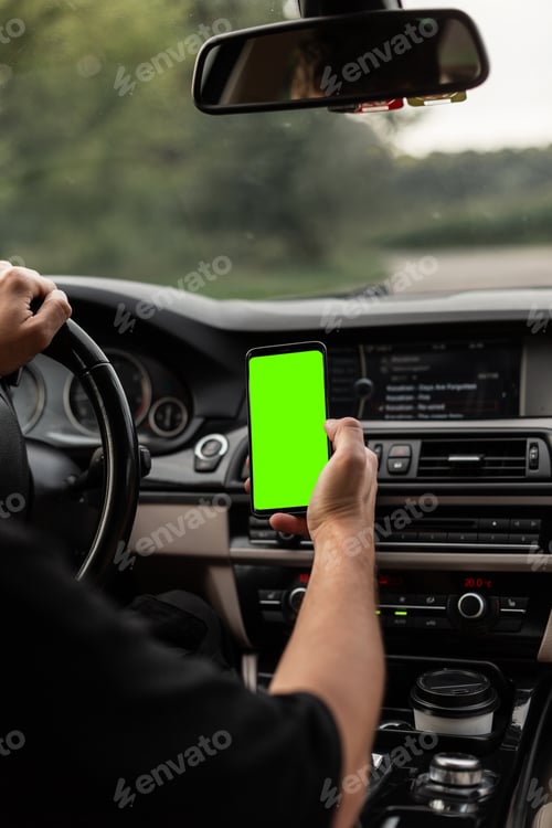 Preview: Man driver is driving and holding a smartphone with a green mockup display.
