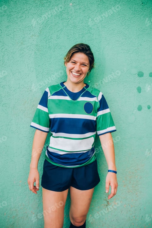 Preview: Young woman smiling in striped sports attire against a green wall