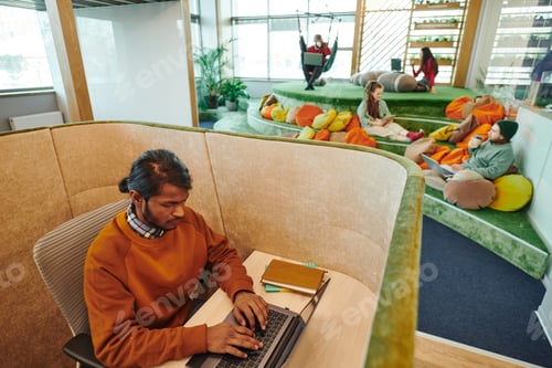 Preview: Young serious mixed-race businessman networking by desk in office environment