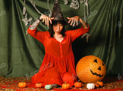 Preview: Portrait of a cute young woman in a red dress and a witch hat at a Halloween party