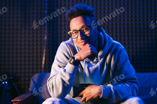 Preview: Portrait young handsome afro man sitting on the couch in neon light