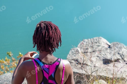 Preview: Back view of young woman in colorful activewear overlooking a beautiful blue lake