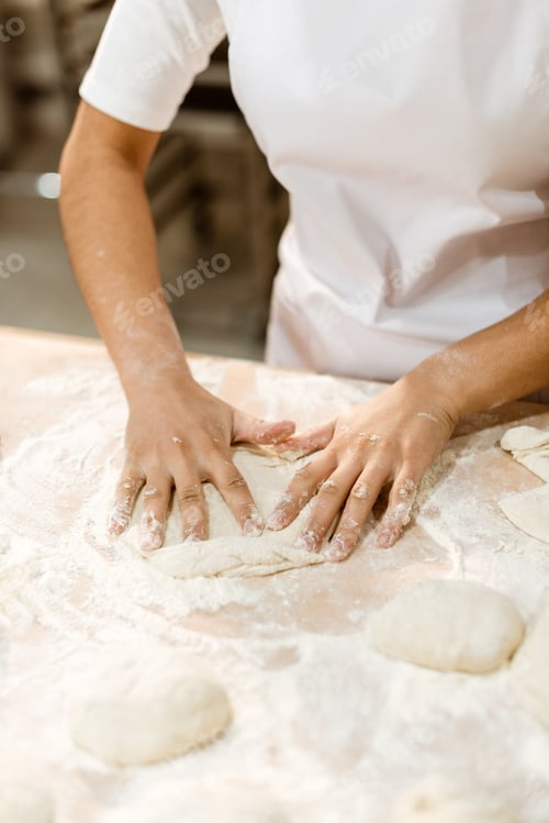 Preview: cropped shot of female baker kneading dough for pastry on messy table