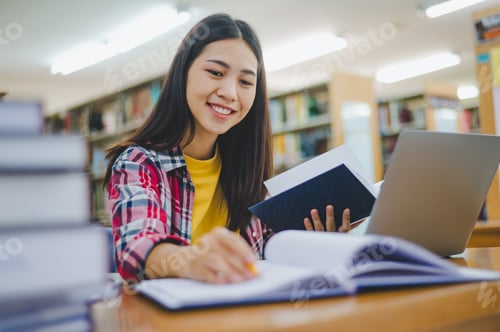 Preview: Female college student working on laptop and searching for books to study