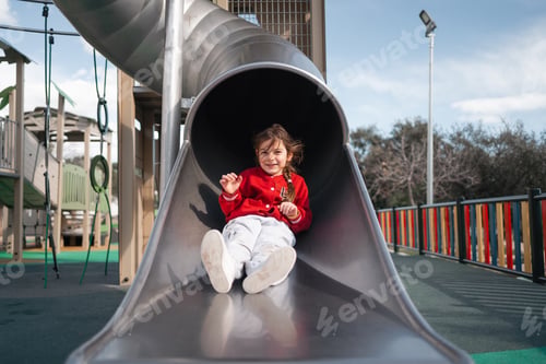 Preview: A happy child sits at the top of a slide in a playground, ready for fun and adventure