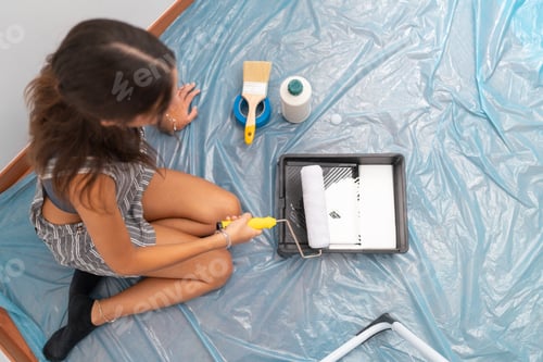 Preview: Top view of a woman using roller to paint the house