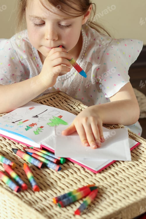 Preview: Little girl 6 years old draws with wax crayons in a sketch book