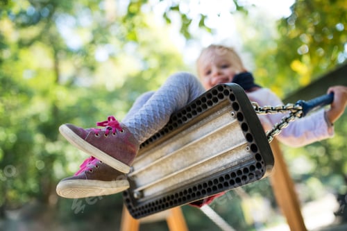 Preview: Low angle view of a small toddler girl on a swing on a playground