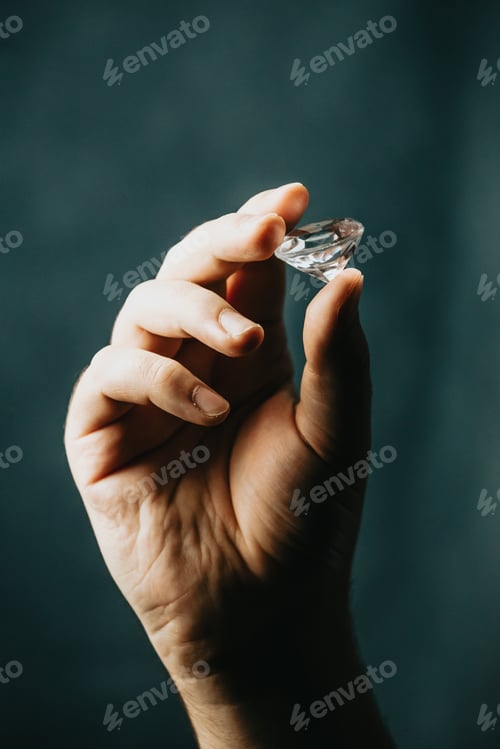 Preview: A hand grabbing a diamond with copy space over a dark background