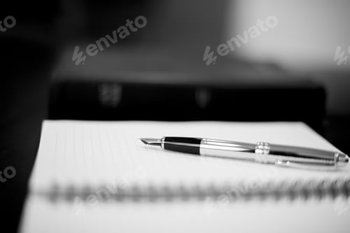 Preview: Grayscale closeup shot of a fountain pen on top of a notebook with a blurred background