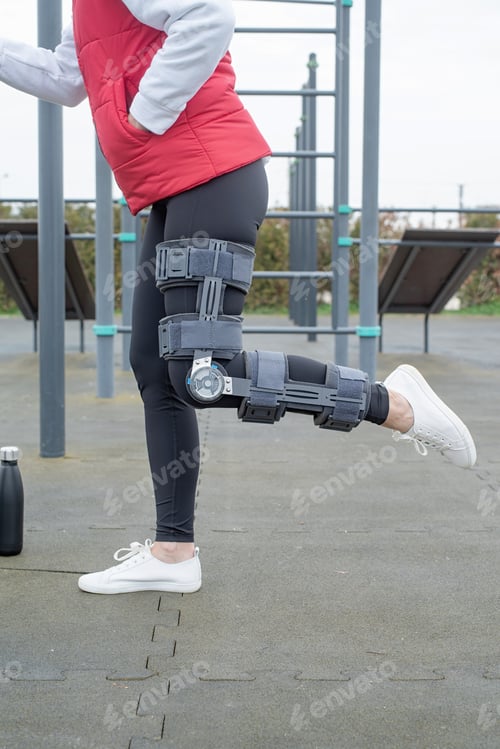 Preview: Woman wearing knee brace or orthosis after leg surgery, walking in the park