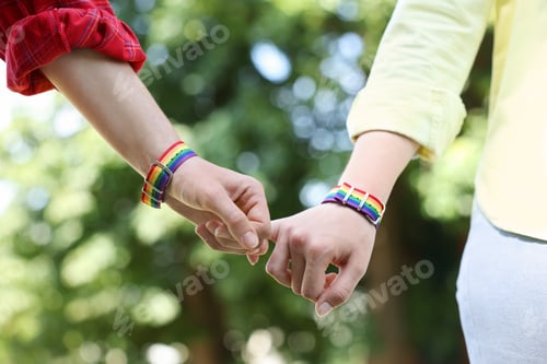 Preview: LGBT concept. Women in rainbow wristbands holding hands outdoors, closeup