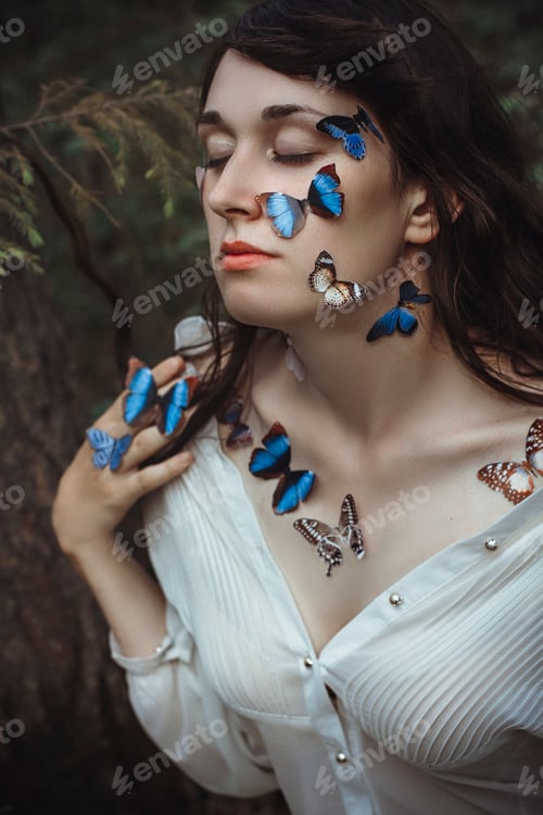 Preview: Beautiful art portrait of a naked woman with blue butterflies on her face and hands near the branch