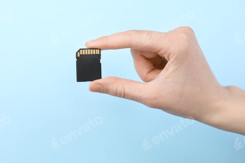 Preview: Woman holding SD memory card on light blue background, closeup