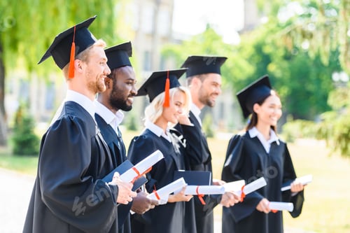 Preview: happy graduated students in capes and hats holding rolled diplomas