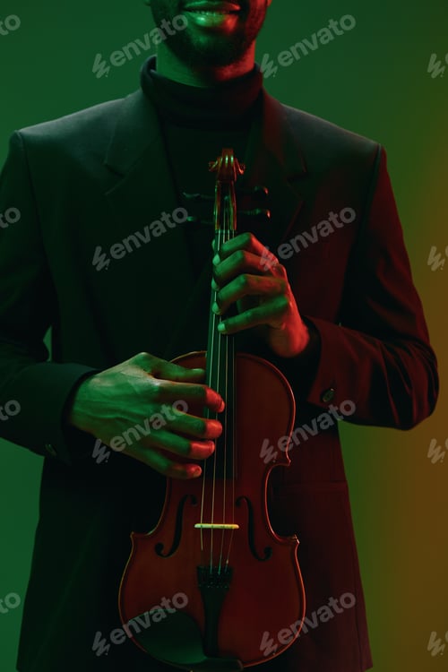 Preview: African American man holding violin against vibrant green and red background for music concept