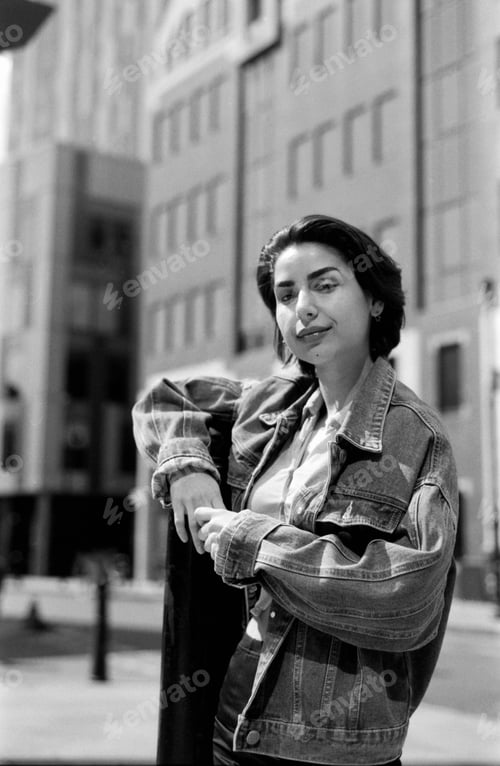 Preview: Young woman posing in urban setting wearing denim jacket, grainy monochrome film aesthetic