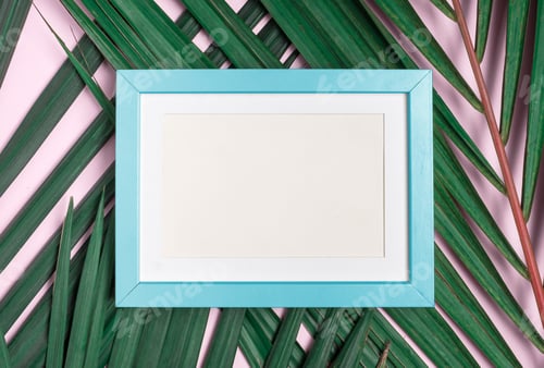 Preview: Top view blank blue pastel photo frame on summer green palm leaf on pastel pink table top background