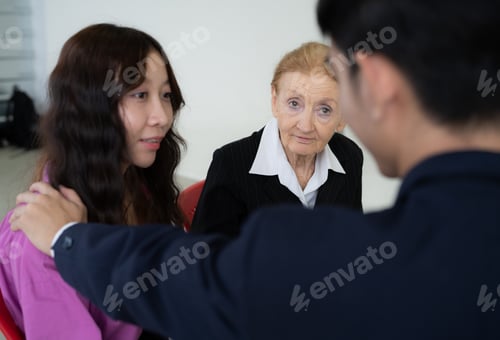 Vista previa: Una mujer con camisa negra y camisa blanca está sentada en una silla con otras dos personas