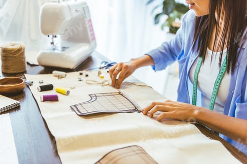 Preview: cropped image of smiling seamstress measuring pattern at table