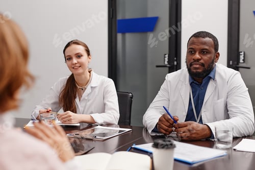 Preview: Two young intercultural healthcare experts in lab coats consulting colleagues