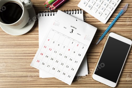 Preview: Work desk setup featuring calendar, notebook, cup of coffee, and smartphone on wooden table