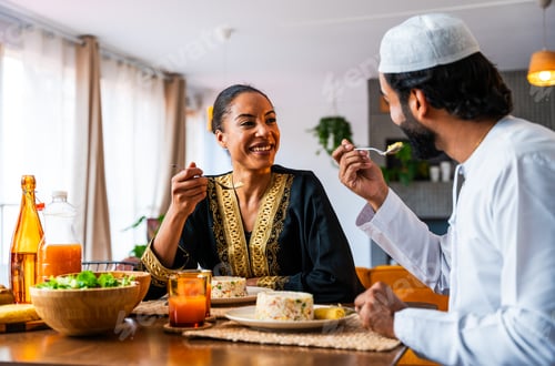 Preview: Happy beautiful young arab couple with emirati clothing having meal together at home