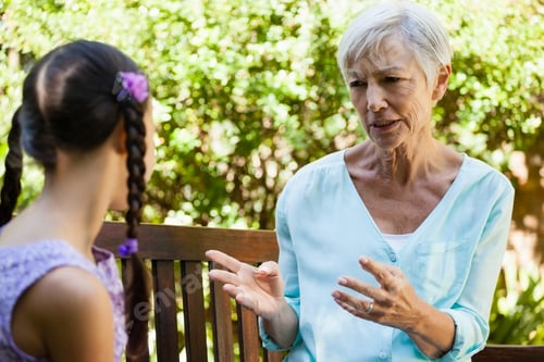 Preview: Senior woman talking with granddaughter while sitting on wooden bench