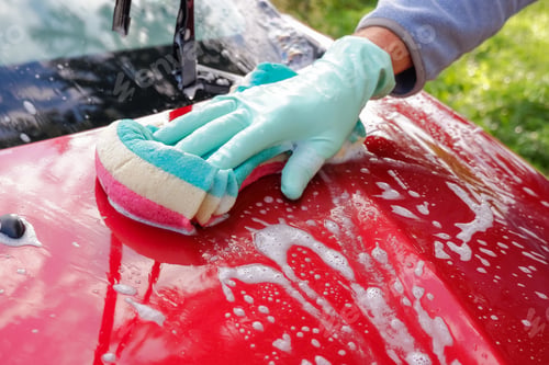 Preview: Worker washing red car with sponge on a car wash.male hand holds with green red sponge washing car