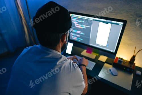 Preview: Young man mobile developer writes program code on a computer, programmer work in home office.