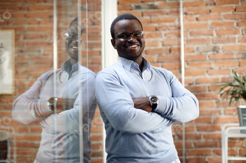 Preview: Portrait of happy African American businessman with arms crossed at corporate office.
