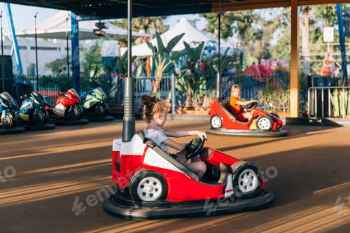 Preview: Two girls, sisters, having fun in the bumper car arena in an amusement park
