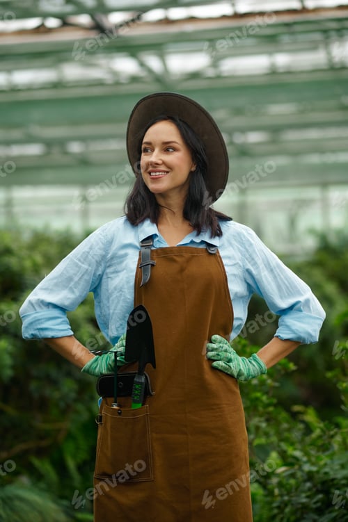 Preview: Young woman gardener proud of beauty of her own greenhouse
