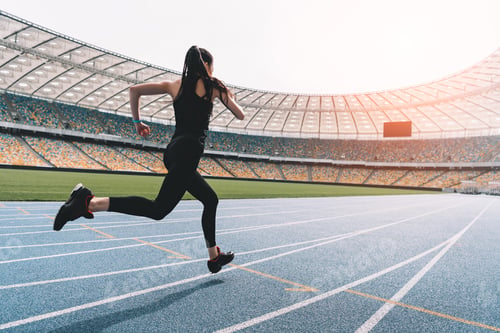 Preview: Athletic young woman in sportswear sprinting on running track stadium at sunset