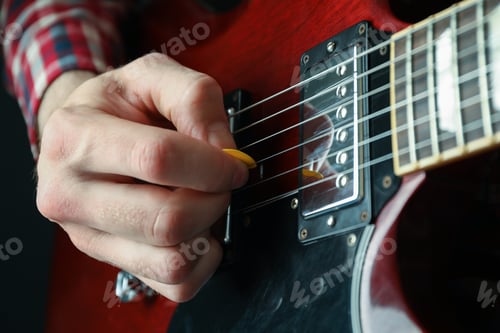 Preview: Man playing on electric guitar against dark background, closeup