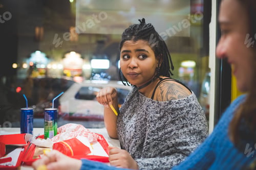 Preview: young african woman eating in restaurant with friends and having conversation