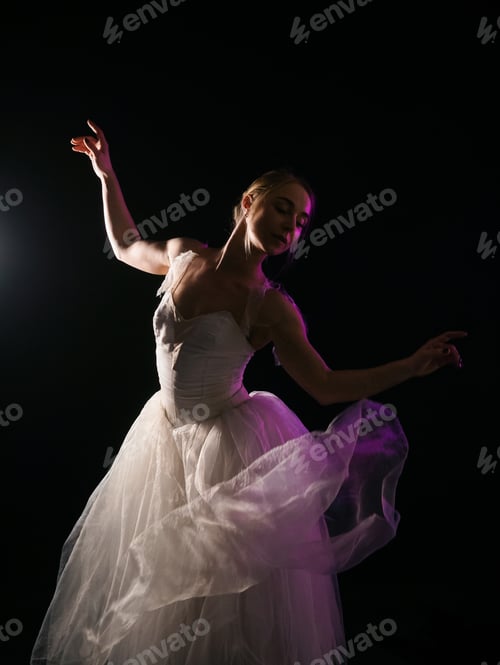 Preview: graceful ballerina in white tutu dress dancing elements of classical or modern ballet in the dark