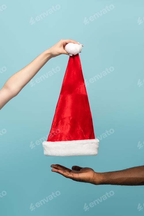 Preview: cropped view of interracial couple holding santa hat isolated on blue background